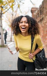Portrait of young afro american woman laughing and holding a cup of coffe in the street. Outdoors.