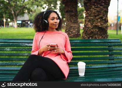 Portrait of young Afro american woman listening to music with headphones and mobile phone in the park. Outdoors.