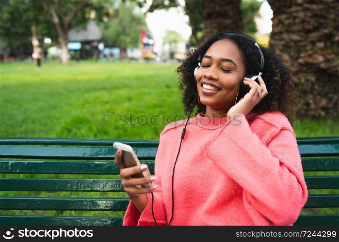 Portrait of young Afro american woman listening to music with headphones and mobile phone in the park. Outdoors.