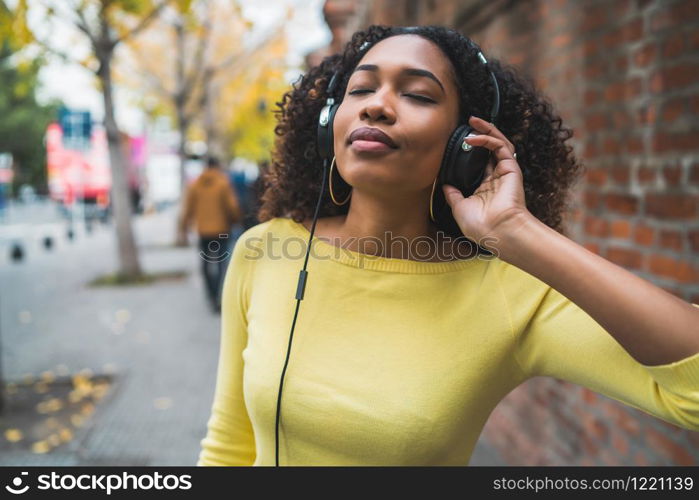 Portrait of young Afro american woman listening to music with headphones in the street. Outdoors.