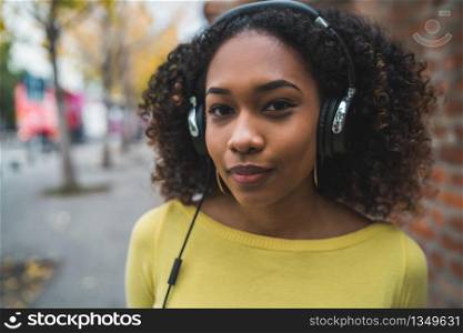 Portrait of young Afro american woman listening to music with headphones in the street. Outdoors.