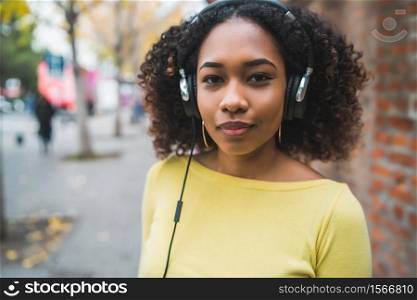 Portrait of young Afro american woman listening to music with headphones in the street. Outdoors.