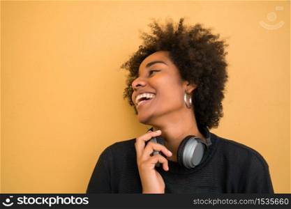 Portrait of young afro american woman looking confident and wearing black headphones against yellow background.