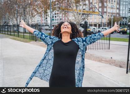 Portrait of young afro american woman standing outdoors with arms raised and laughing.