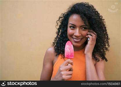 Portrait of young afro american woman talking on the phone while eating ice-cream. Communication and lifestyle concept.