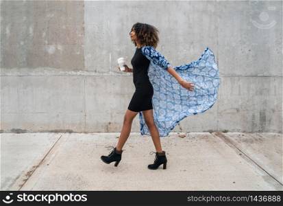 Portrait of young afro american woman walking and holding a cup of coffee. Outdoors.