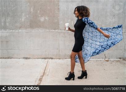 Portrait of young afro american woman walking and holding a cup of coffee. Outdoors.