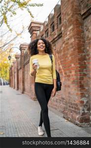 Portrait of young afro american woman walking on the street and holding a cup of coffee. Outdoors.
