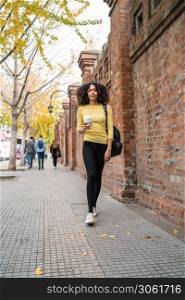 Portrait of young afro american woman walking on the street and holding a cup of coffee. Outdoors.