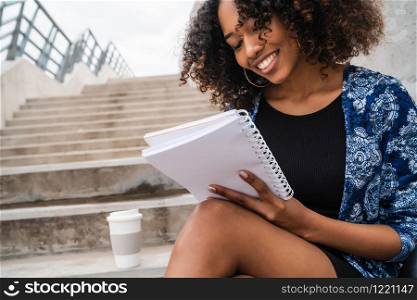 Portrait of young afro-american woman writing in a notebook while sitting outdoors on stairs.