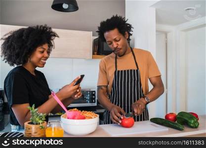 Portrait of young afro couple cooking together in the kitchen while woman taking photo of food with phone at home. Relationship, cook and lifestyle concept.. Afro couple cooking together in the kitchen.
