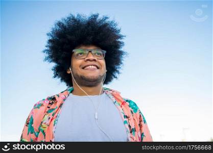 Portrait of young afro latin man listening music with earphones while standing outdoors on the street. Urban concept.