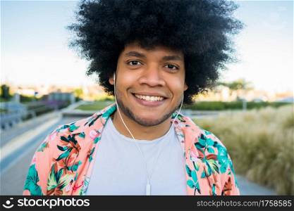 Portrait of young afro latin man smiling and looking at camera while standing outdoors on the street. Urban concept.