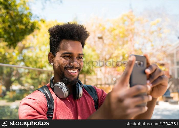 Portrait of young afro man taking selfies with his mophile phone outdoors in the street. Technology concept.