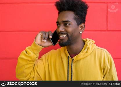 Portrait of young afro man talking on the phone against red wall. Communication and technology concept.