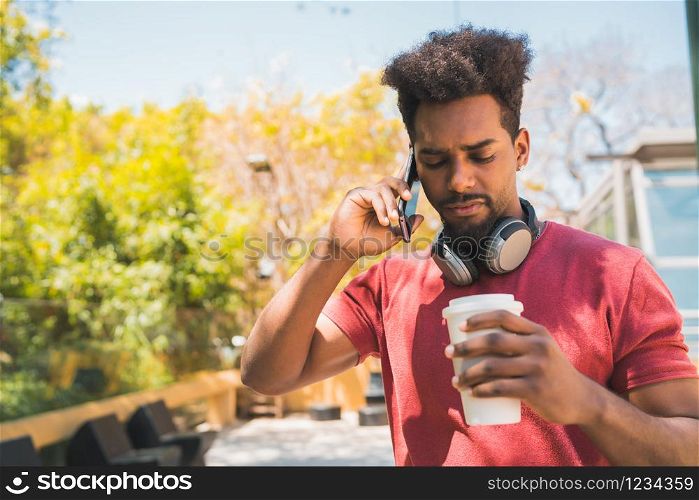 Portrait of young afro man talking on the phone while holding a cup of coffee outdoors. Communication, lifestyle and urban concept.