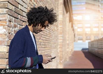 Portrait of young afro man using his mobile phone against brick wall. Technology and lifestyle concept.