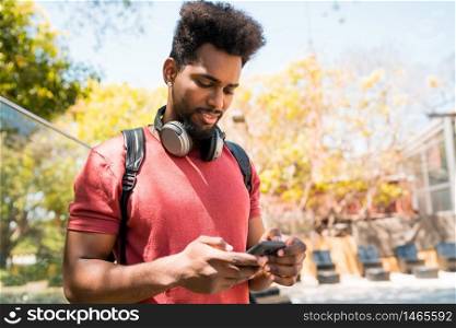 Portrait of young afro man using his mobile phone outdoors. Technology, urban and lifestyle concept.