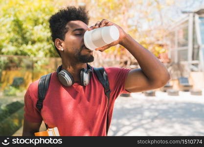 Portrait of young afro university student holding his books and drinking a cup of coffee outdoors in the campus. Education and lifestyle concept.