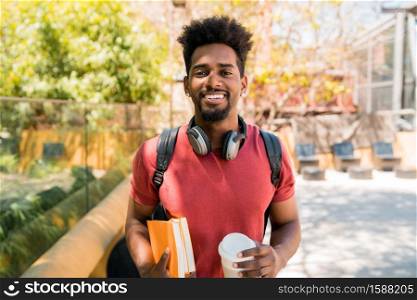 Portrait of young afro university student holding his books and looking at camera, outdoors in the campus. Education and lifestyle concept.