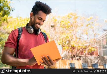 Portrait of young afro university student reading and studying with his book on the campus. Education and lifestyle concept.