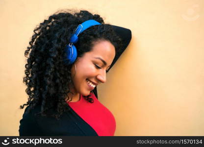 Portrait of young afro woman enjoying and listening to music with blue headphones. Technology and lifestyle concept.