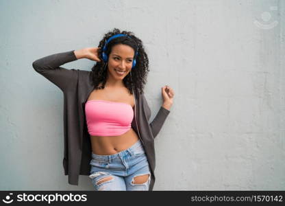 Portrait of young afro woman enjoying and listening to music with blue headphones. Technology and lifestyle concept.