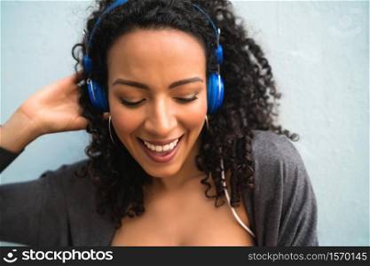 Portrait of young afro woman enjoying and listening to music with blue headphones. Technology and lifestyle concept.
