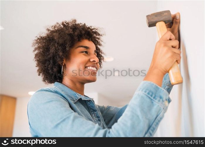 Portrait of young afro woman hammering nail on the wall at home. Home improvement and repair home concept.