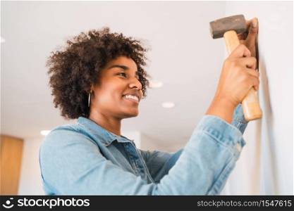 Portrait of young afro woman hammering nail on the wall at home. Home improvement and repair home concept.