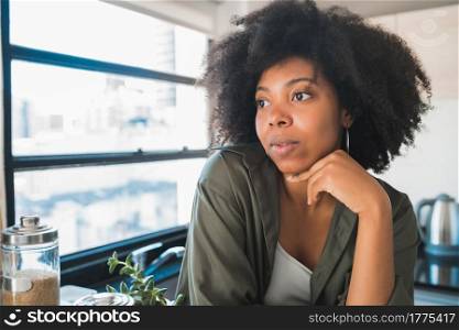 Portrait of young afro woman relaxing and looking pensative at home. Lifestyle concept.