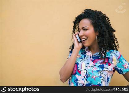 Portrait of young afro woman talking on the phone against yellow background. Communication concept.
