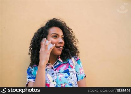 Portrait of young afro woman talking on the phone against yellow background. Communication concept.