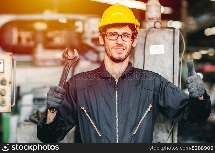 Portrait of young American happy worker enjoy happy smiling to work in a heavy industrial factory.Thumb up with big wrench.