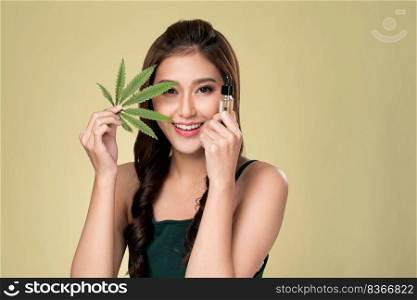 Portrait of young ardent woman with healthy fresh skin holding green hemp leaf and cbd oil. Combination of beauty and cannabis concept.. Young ardent woman with healthy skin holding green hemp leaf and cbd oil.