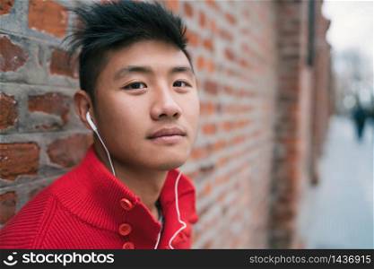 Portrait of young Asian boy listening to music with earphones outdoors in the streetl. Urban concept.
