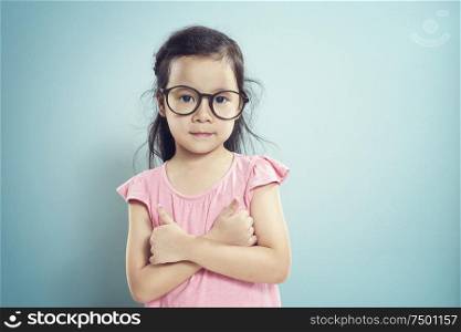 Portrait of young asian little cute girl shows a thumbs up by two finger pose . Vintage mint green wall background.