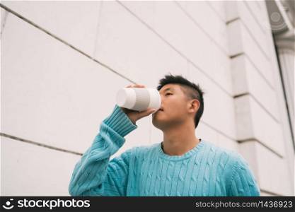 Portrait of young Asian man drinking a cup of coffee while walking outdoors in the street. Urban concept.