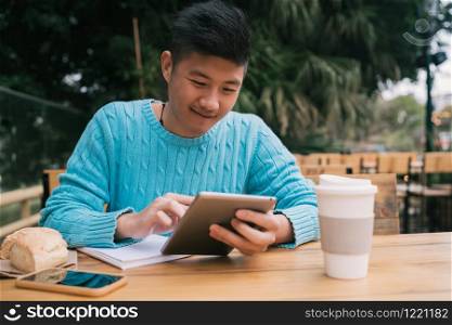 Portrait of young Asian man studying with his digital tablet while sitting in a coffee shop. Technology concept.