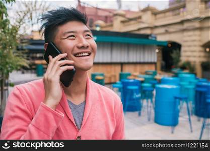 Portrait of young Asian man talking on the phone outdoors. Communication concept.