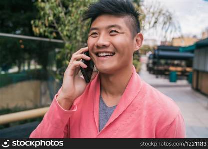 Portrait of young Asian man talking on the phone outdoors in the street. Communication concept.