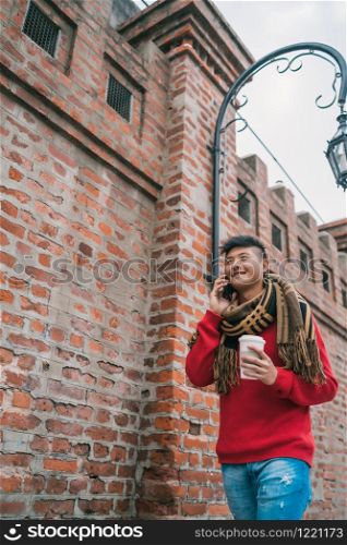 Portrait of young Asian man talking on the phone while walking outdoors in the street. Communication concept.