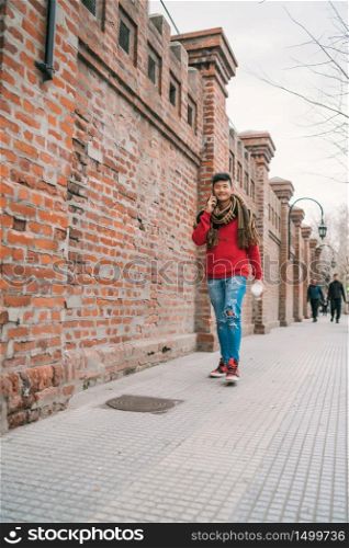 Portrait of young Asian man talking on the phone while walking outdoors in the street. Communication concept.