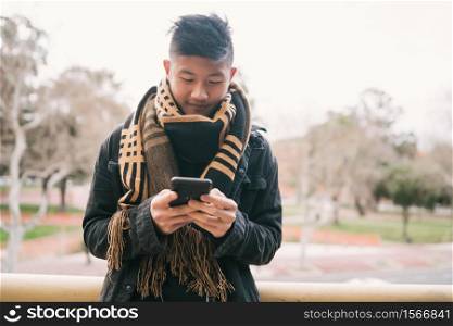 Portrait of young Asian man using his mobile phone standing outdoors in the street. Communication concept.