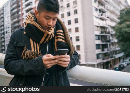 Portrait of young Asian man using his mobile phone standing outdoors in the street. Communication concept.