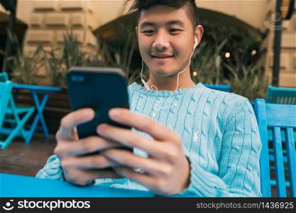 Portrait of young Asian man using his mobile phone with earphones while sitting in a coffee shop. Communication concept.