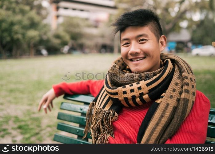 Portrait of young Asian man wearing winter clothes and relaxed sitting on a bench in a park.