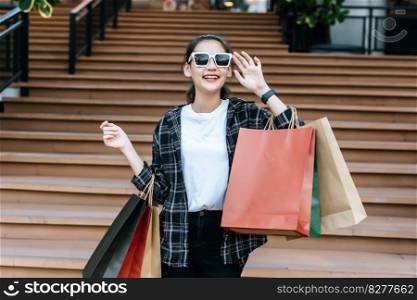 Portrait of young Asian woman in face mask wearing eyeglasses standing on stairs with shopping paper bag. she smile with happy, New normal Lifestyle and shopping concept