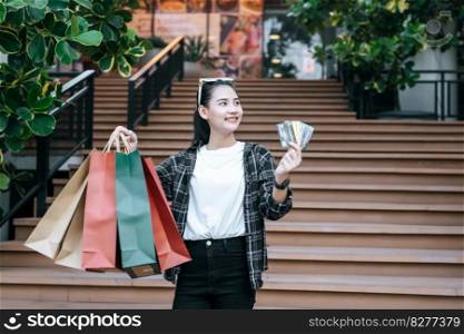 Portrait of young Asian woman in protection mask, eyeglasses on head standing with multi color shopping paper bag and show three credit cards in hand,  Lifestyle and shopping concept, copy space