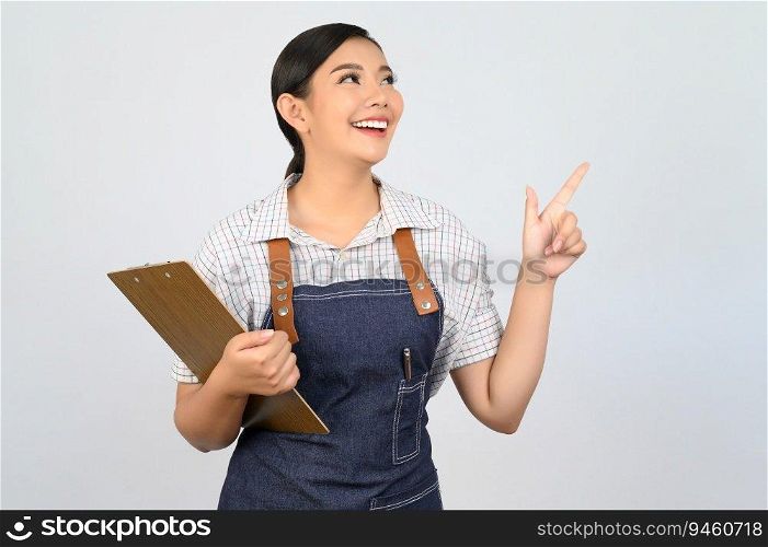 Portrait of young asian woman in waitress uniform holding clipboard and point finger, copy space to insert products for advertisement isolated on white background